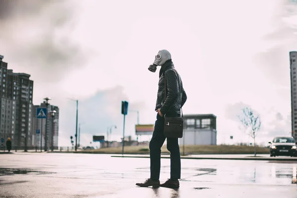 Casual jongeman in een gasmasker staan op straat in een geïnfecteerde stad. — Stockfoto