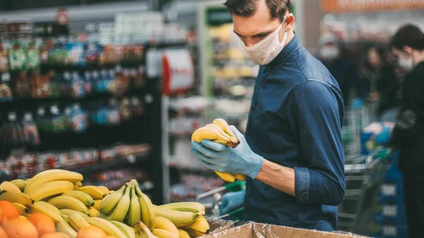 Customer in protective gloves choosing bananas in a supermarket — Stock Photo, Image