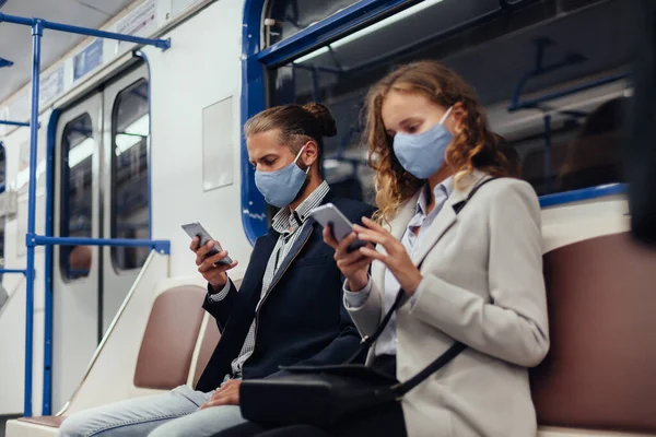 Passageiros usando máscaras protetoras usando seus smartphones enquanto sentados em um carro de metrô. — Fotografia de Stock