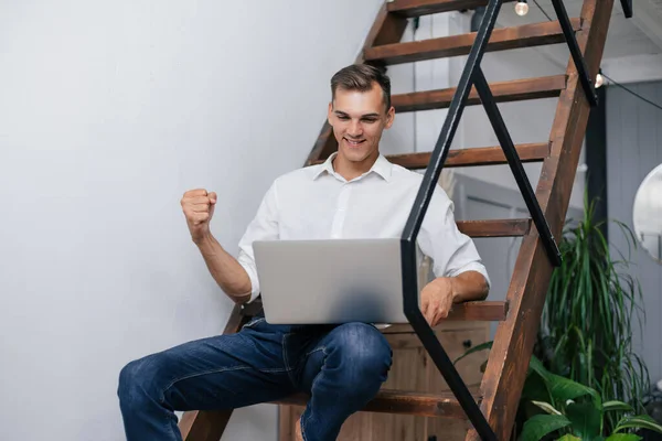 Glücklicher Mann mit Laptop auf den Stufen in seiner Wohnung. — Stockfoto