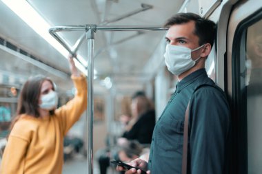 Koruyucu maskeli genç adam akıllı telefonunun ekranına bakıyor.