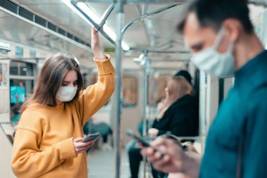 Metro vagonunda duran koruyucu maskeli genç bir kadın..