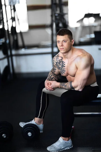 Joven culturista sentado en un banco en el gimnasio. —  Fotos de Stock