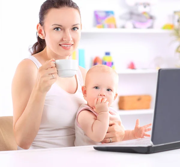 Jovem mãe com bebê sentado na frente de um laptop aberto. — Fotografia de Stock