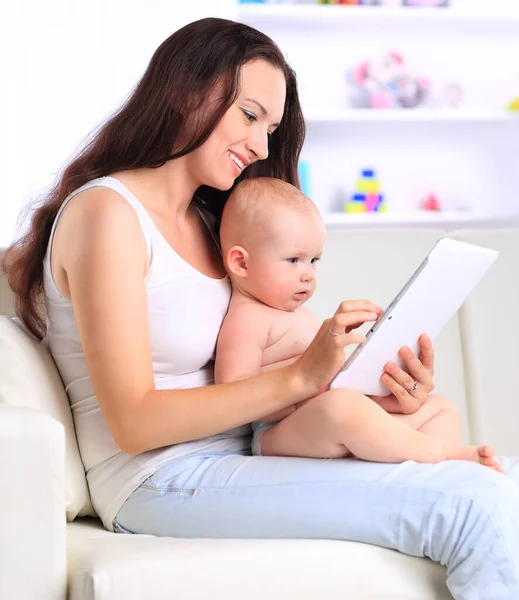 Jovem mãe com seu bebê olhando para a tela de um tablet digital. — Fotografia de Stock