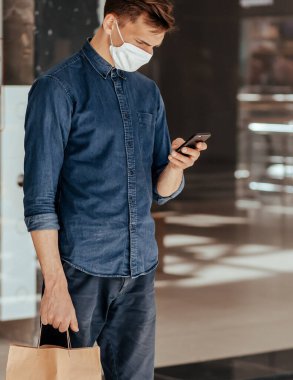 Elinde alışveriş çantası olan bir adam akıllı telefonundan mesaj okuyor..