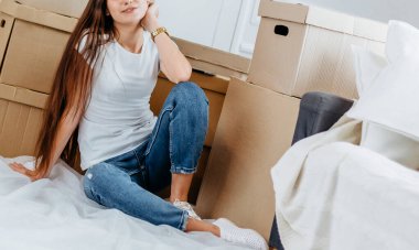 Mutlu genç bir kadın yeni dairesinde yerde oturuyor.