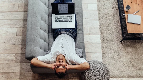 stock image happy man with a laptop lying on the couch .