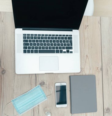 Ofis masasında bilgisayar, akıllı telefon ve koruyucu maske.