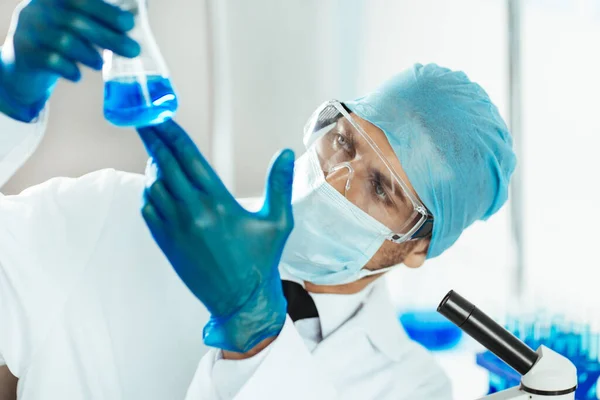 Cientista em vestuário de protecção que olha para o líquido no frasco. — Fotografia de Stock