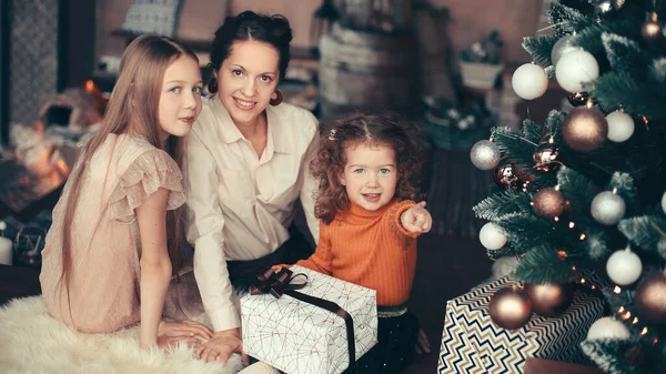 Moeder en haar dochters openen een geschenkdoos bij de kerstboom — Stockfoto