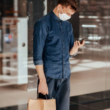 Alışveriş çantalı bir adam akıllı telefonunun ekranına bakıyor..