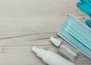 Dezenfekte sıvısı, sprey, koruyucu maske ve eldivenler ahşap bir masada.