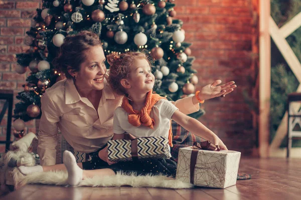 Klein meisje kust haar moeder in de buurt van de kerstboom — Stockfoto