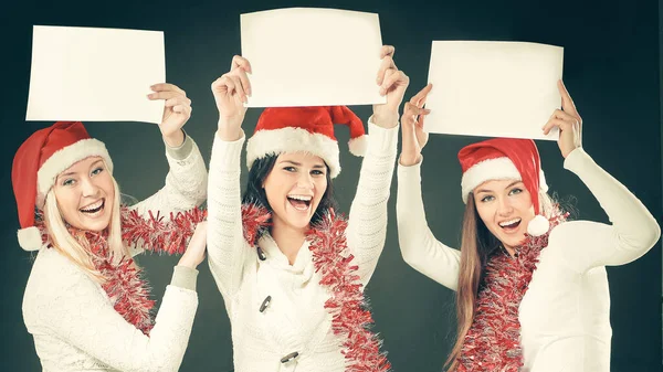 Noel Baba kostümlü üç genç kız boş çarşaf gösteriyor. — Stok fotoğraf