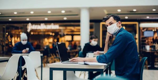 Homme dans un masque de protection travaille sur un ordinateur portable assis à une table dans un café. — Photo