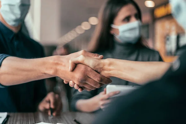 Zakenman met een beschermend masker knijpt in de hand van zijn collega. — Stockfoto