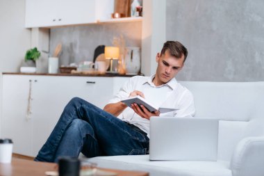 Genç adam kanepede oturmuş notlar alıyor. .