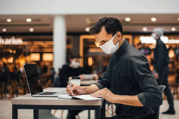 Jeune homme avec un ordinateur portable travaille assis à une table dans un café — Photo