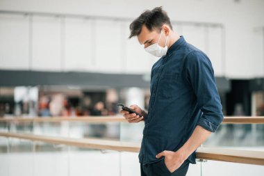 Koruyucu maskeli genç bir adam, kolunda bir mesaj okuyor.