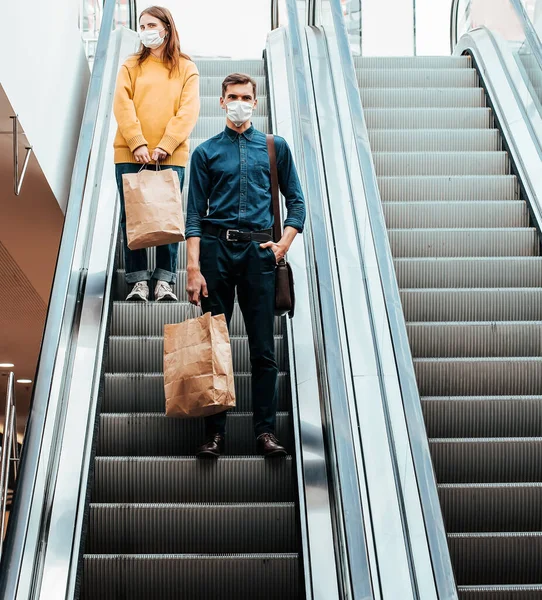 一个戴着防护面具的年轻人站在购物中心的自动扶梯上 — 图库照片