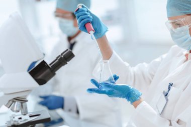 Kapat. Kadın bilim adamı bir laboratuvar şişesinde sıvı inceliyor. .