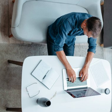 Genç adam evinde dizüstü bilgisayarla çalışıyor..