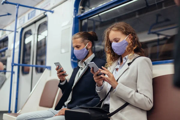 Passageiros usando máscaras protetoras usando seus smartphones enquanto sentados em um carro de metrô. — Fotografia de Stock