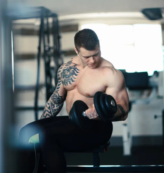 Μυώδης bodybuilder με αλτήρες κάθεται σε ένα παγκάκι στο γυμναστήριο — Φωτογραφία Αρχείου