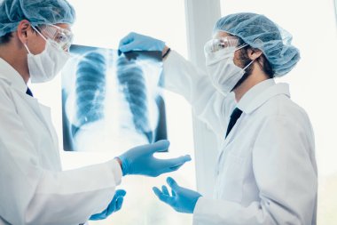 Kapat. Koruyucu maskeli bilim adamları akciğerlerin röntgenine bakıyor. .