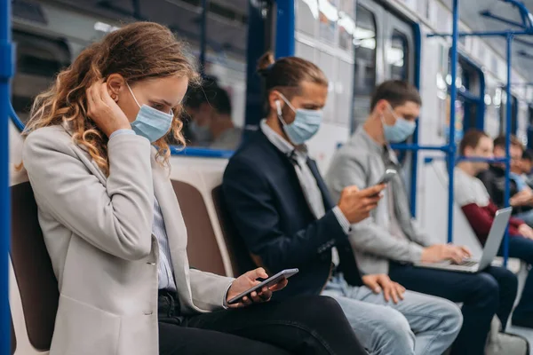 Passageiros em máscaras de proteção usando seus gadgets no carro do metrô . — Fotografia de Stock