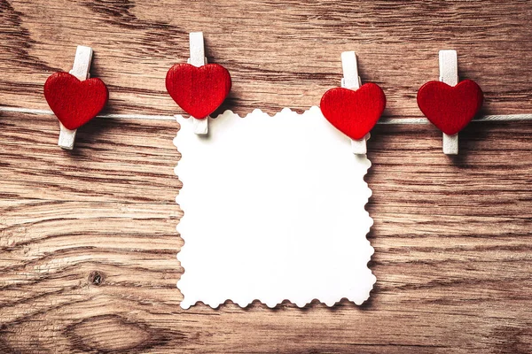 Corazones y nota en blanco en el tendedero sobre fondo de madera. — Foto de Stock