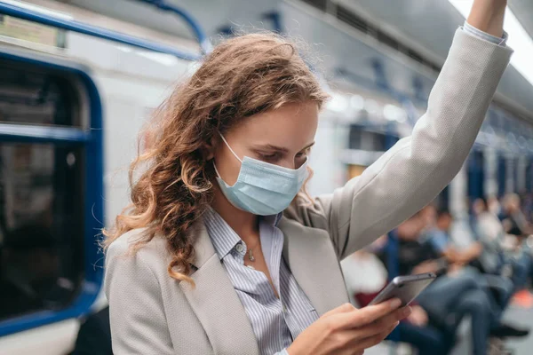 Jovem mulher em uma máscara protetora em pé em um trem de metrô. — Fotografia de Stock