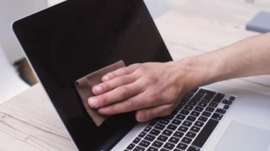 Adam dizüstü bilgisayarının ekranını ve klavyesini dezenfekte beziyle siliyor. Kapat - kapat .