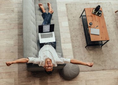 Oturma odasındaki kanepede dizüstü bilgisayarı olan yorgun bir adam. .