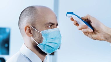 Koruyucu maskeli adam sıcaklığı dijital termometreyle ölçüyor..
