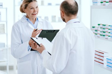 Erkek ve kadın eczacılar yeni ilaçları tartışıyor.