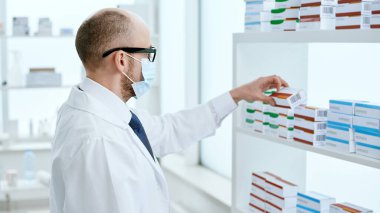 Koruyucu maskeli eczacı yeni bir ilaç kutusu alıyor. .