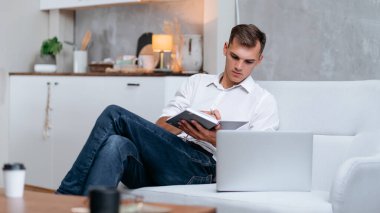 Genç adam kanepede oturmuş notlar alıyor. .