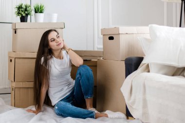 Mutlu genç bir kadın yeni dairesinde yerde oturuyor.