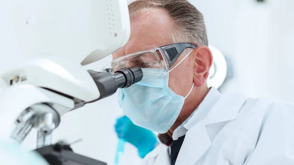 scientist in a protective mask looking through a microscope.