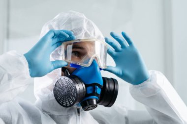 Koruyucu tulumlu adam, gözlüklerini ayarlıyor..