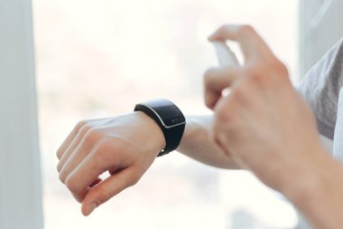 Genç adam akıllı saatine alkol antiseptiği püskürtüyor..