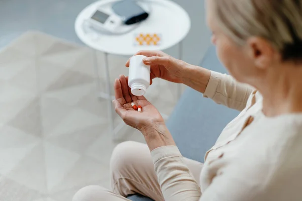 mature lady taking medicine sitting on the couch .