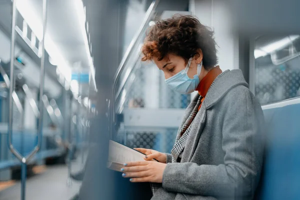 Femme dans un masque de protection lit un livre dans un train de métro. — Photo