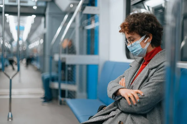 Mulher cansada em uma máscara protetora dorme em um carro de metrô vazio . — Fotografia de Stock