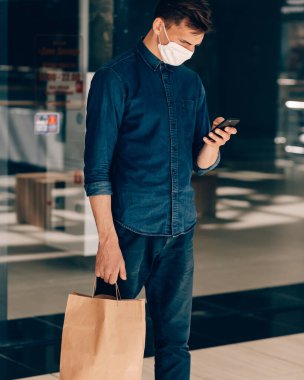 Elinde alışveriş çantası olan bir adam akıllı telefonundan mesaj okuyor..