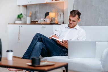 Genç adam kanepede oturmuş notlar alıyor. .