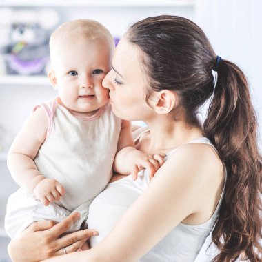 Bir çocuk odasının arka planında kollarında bir bebek olan mutlu bir annenin portresi.