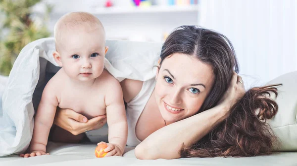 Concepto de madres felices: madre feliz y su hijo de años jugando en el sofá en el dormitorio — Foto de Stock